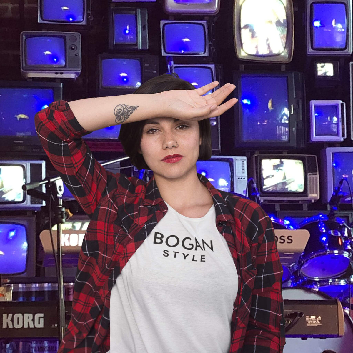 Girl standing in front of a wall of televisions wearing Bogan Style t shirt and flanno