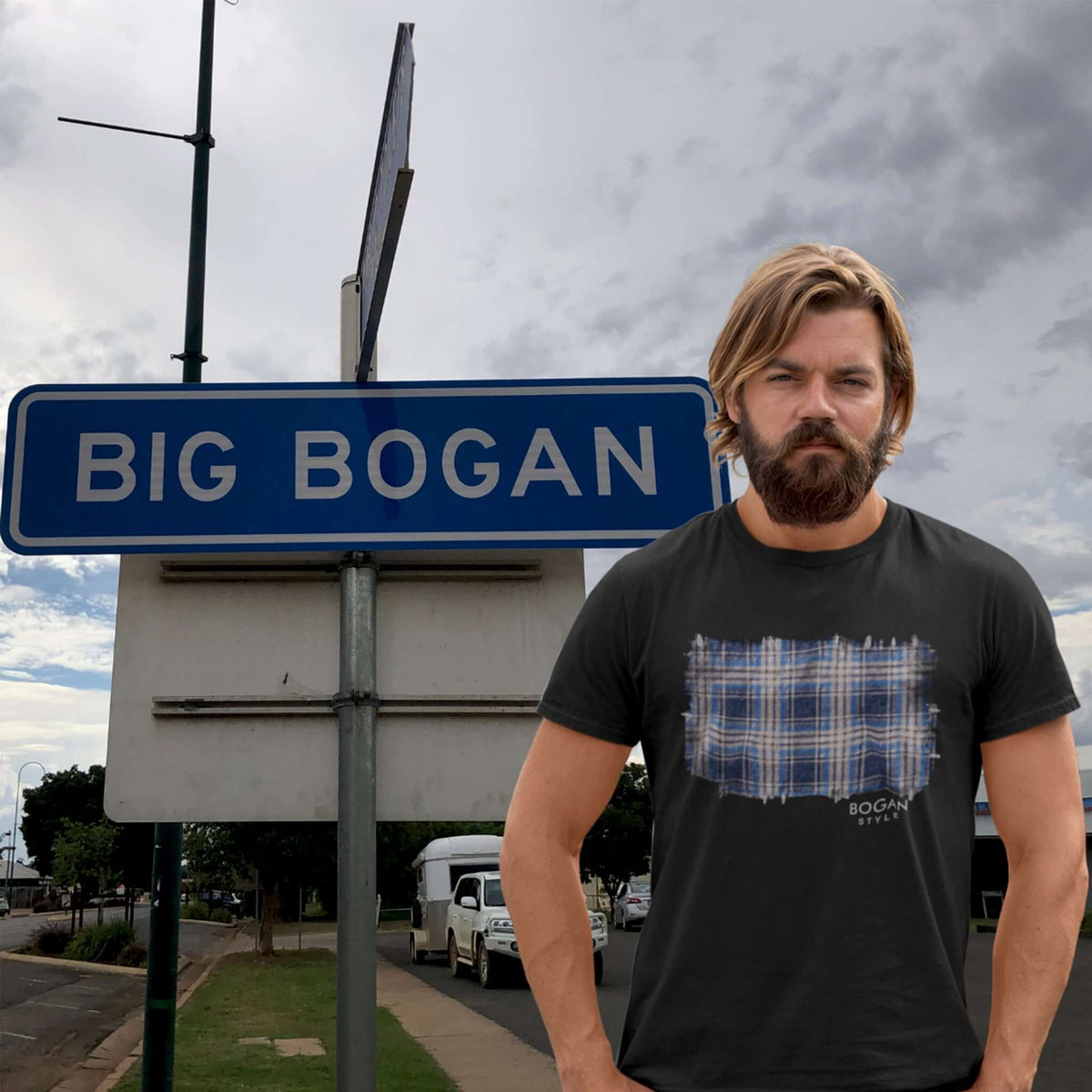 Man stands in front of Big Bogan sign wearing black tee with flanno design on front